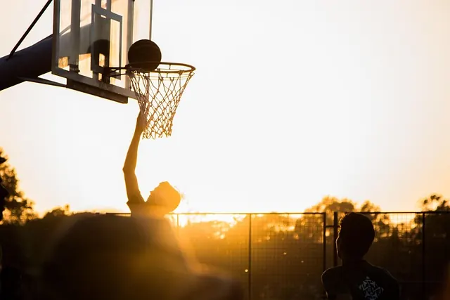 A player laying the ball up at an outdoor hoop with the sun low behind them
