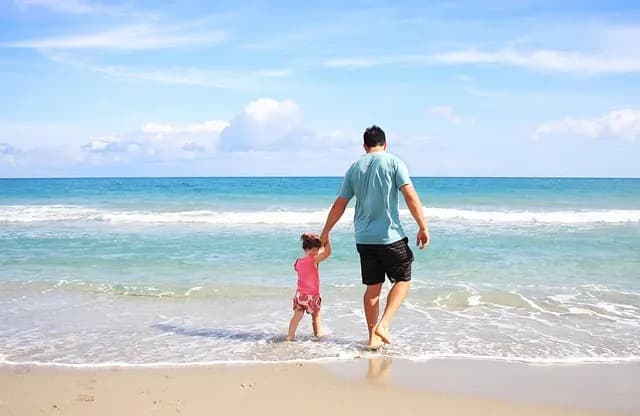 A father and his young daughter holding hands as they walk into the surf